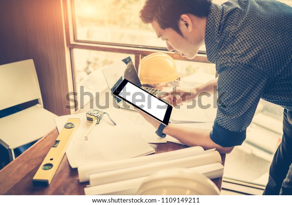 Architect working on blueprint.\
Architects workplace - architectural project, blueprints, tablet\
pc. Construction concept. Engineering tools. Copy space for\
text.