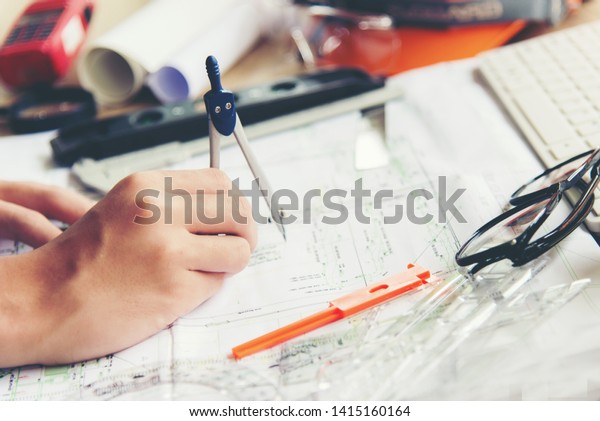 Architect working\
on blueprint. Architects workplace.  Engineer tools and safety\
control,  blueprints, ruler, orange helmet,radio,laptop and divider\
compass. Construction\
Concept.