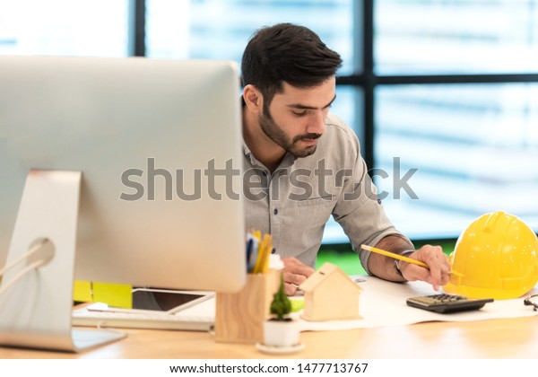 Architect working on blueprint. Architects\
workplace. Engineer tools and safety control, blueprints, ruler,\
orange helmet,radio,laptop and divider compass. Construction\
Concept. select\
focus\

