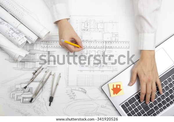 Architect working on blueprint. Architects workplace\
- architectural project, blueprints, ruler, calculator, laptop and\
divider compass. Construction concept. Engineering tools. Top\
view