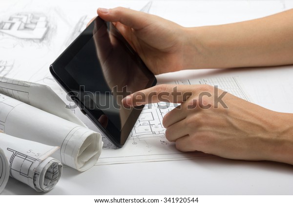 Architect working\
on blueprint. Architects workplace - architectural project,\
blueprint roll, plan, blank tablet pc. Construction concept.\
Engineering tools. Cope space for\
text.