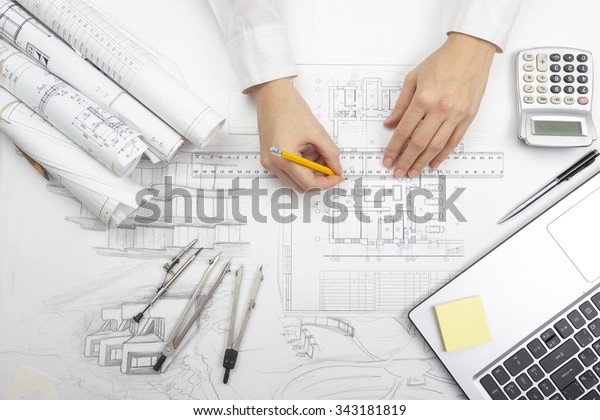Architect working on blueprint. Architects workplace\
- architectural project, blueprints, ruler, calculator, laptop and\
divider compass. Construction concept. Engineering tools. Top\
view