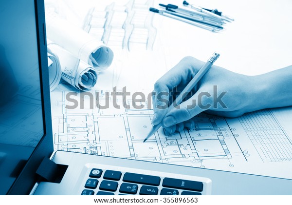 Architect working on blueprint. Architects\
workplace - architectural project, blueprints, laptop. Construction\
concept. Engineering tools. Toned\
image