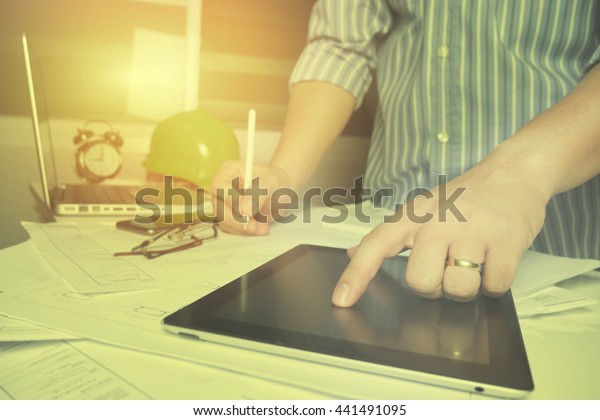 Architect working on blueprint.  At Architects\
workplace,architectural project, blueprints, ruler, tablet pc,\
laptop and divider compass. Construction. Engineering\
tools.selective focus,vintage\
color