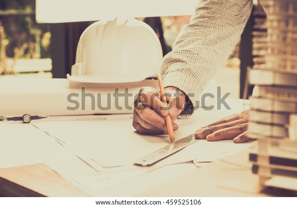 Architect working on blueprint.\
Architects workplace - architectural project, blueprints, ruler,\
helmet and divider. Construction concept. Engineering\
tools