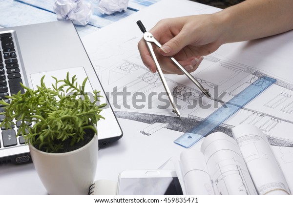 Architect working on blueprint. Architects\
workplace - architectural project, blueprints, ruler, calculator,\
laptop and divider compass. Construction concept. Engineering\
tools. Top view.