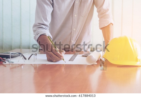 Architect working on blueprint.\
Architects workplace - architectural project, blueprints, ruler,\
helmet and divider. Construction concept. Engineering\
tools