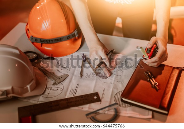 Architect working on blueprint. Architects\
workplace - architectural project, blueprints, ruler, calculator,\
laptop and divider compass. Construction concept. Engineering\
tools,selective focus
