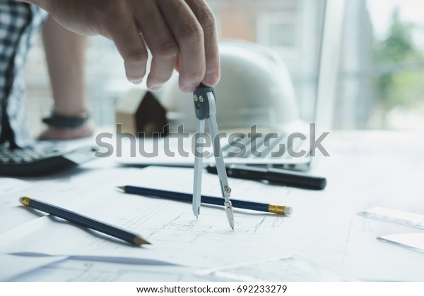 architect working on real estate project at
workplace. Engineer using divider compass at office. Male hand
working with living house blueprint. Business, people, construction
and building concept