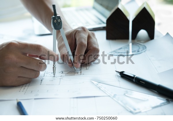 architect working on real estate project at
workplace. Engineer using divider compass at office. Male hand
working with living house blueprint. Business, people, construction
and building concept