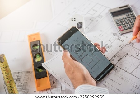 Architect workplace. Architectural building design and construction plans with blueprints paper project plans, designing man edit building or architecture online check by smart mobile phone screen