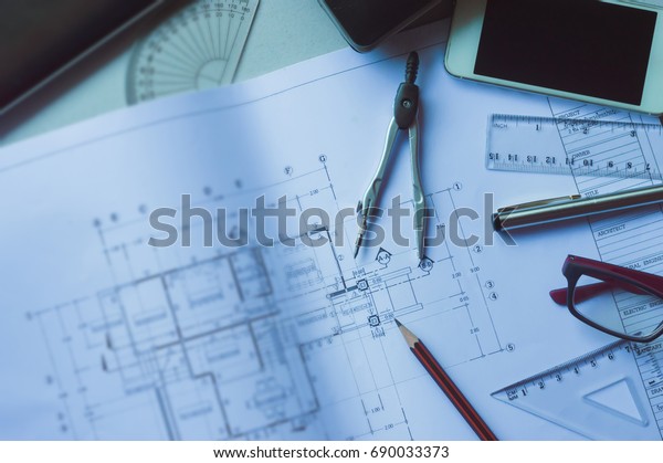 The\
architects \'and engineers\' desks with Divider, pencil, pen, ruler,\
glasses and smartphone and blueprint on table top.Table top view of\
Engineers table at office workplace.selective\
focus.