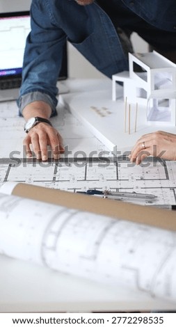 Architects collaborating on building design, a female showing a colleague a blueprint layout while creating a physical architectural model in an office