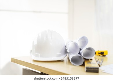 An architect's desk with blueprints and a white hardhat sits empty, ready for the next project. No people are present, highlighting the tools of the trade. - Powered by Shutterstock