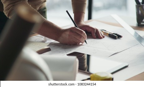 Architect's desk: drawings, tape measure, ruler and other drawing tools. Engineer works with drawings in a bright office, close-up. Insturments and office for designer. Male hands draw with a pencil.