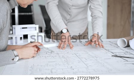 Architects are discussing building plans, using a compass over blueprints while collaborating on a new construction project in an office, emphasizing design, planning, and teamwork, close up