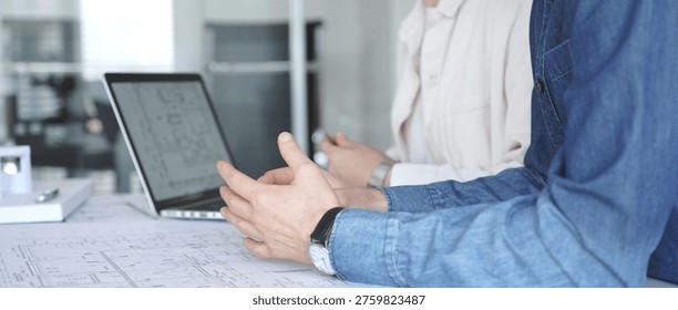 Architects and engineers collaborating on a technical blueprint, discussing construction plans and urban planning details during an office meeting with a laptop displaying cad drawings