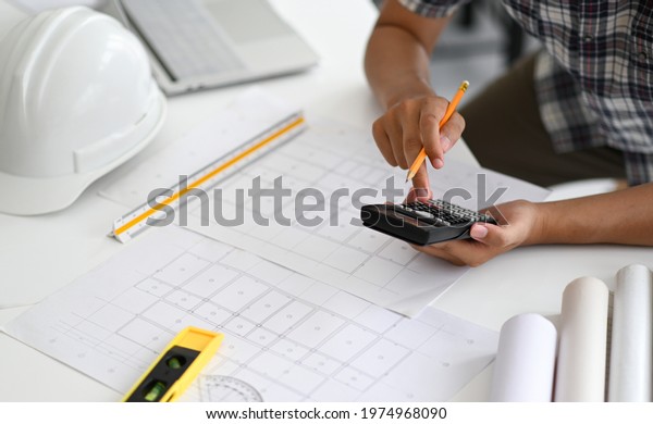 Architects are using a calculator to estimate the\
cost of house plans, house plans, safety helmet and office\
equipment placed on the\
desk.
