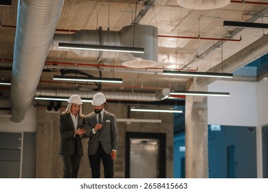 Architects using a digital tablet are discussing a construction project while walking in a building under construction