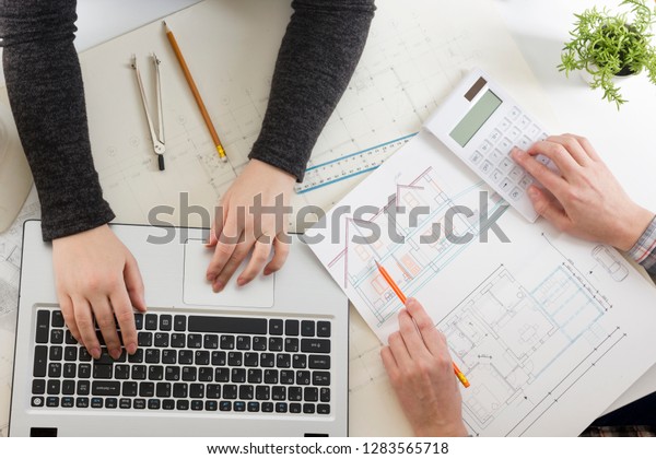 Architects working on blueprint, real estate\
project. Architect workplace - architectural project, blueprints,\
ruler, calculator, laptop and divider compass. Construction\
concept. Engineering\
tools.