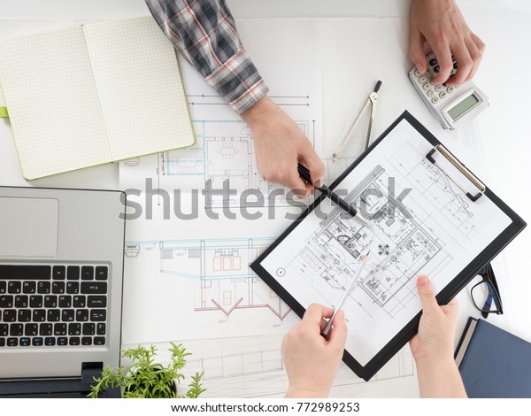 Architects working on blueprint, real estate\
project. Architect workplace - architectural project, blueprints,\
ruler, calculator, laptop and divider compass. Construction\
concept. Engineering\
tools.