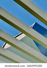 Architectural abstract with diagonal lines. View of a modern building facade through a metal pergola against a blue sky.