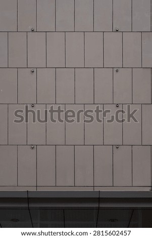 Architectural background of beige vertical cladding panels with exposed metal bolts on a building exterior.