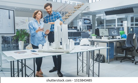 In Architectural Bureau: Architect And Engineer Talking, Using Digital Tablet Computer, Working On A Building Complex Prototype Project, Using City Model And Computers Running 3D CAD Software