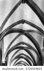 Architectural ceiling design featuring gothic arches with intricate stone carvings, creating a dramatic effect in black and white. Ideal for backgrounds or design themes.