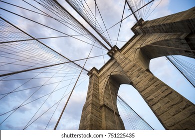 Architectural close-up detail of the landmark Brooklyn Bridge in New York City with its iconic steel cables making criss-cross patterns against a sunset sky - Powered by Shutterstock