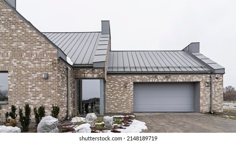 Architectural Detail For Building, Single Family House. Roof Made Of Aluminum Sheet In Gray Color. Walls Made Of Brick And Window Woodwork In Grey Color. British Style Of The Building. 