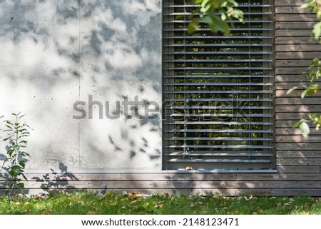 Architectural detail on a section of the facade of a single family home made of wood and concrete. Visible window with aluminium facade shutters