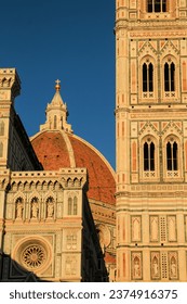 Architectural details of Florence Cathedral (Duomo di Firenze) showcasing its iconic red dome and ornate campanile bathed in golden sunlight against a clear sky.