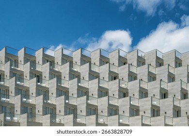 Architectural elements of modern apartment complex. Geometric pattern of balconies and windows creating rhythmic facade design. Contemporary urban architecture against blue sky, exterior detail.