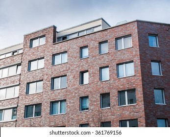 Architectural Exterior Detail Of Low Rise Residential Apartment Building With Brick Facade With Uniform Windows And Overcast Sky In Background