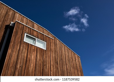 Architectural Features Of A Modern House With Wood Cladding And A Window Against A Blue Sky With A Cloud.