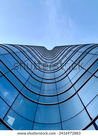 An architectural photograph looking up at a curving glass skyscraper, with its facade reflecting the blue sky and creating a wave-like effect [[stock_photo]] © 