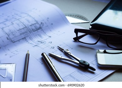 Architectural plan,Divider,pencil,pen,ruler, glasses and smartphone and blueprint on table top.Top view of Engineers table at office workplace.selective focus.Engineering house drawings and blueprint.