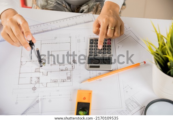 Architectural project workplace. Architect\
drawing with divider compass on house plan blueprint paper for\
repair tools on table desk at architecture office, Engineer\
sketching construction\
project