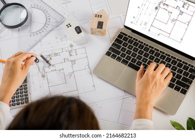 Architectural project workplace. Architect typing laptop keyboard to review design of house before editing or sketching with compass on plan blueprint paper on table desk at architecture office