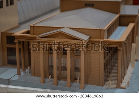 Architectural scale model of a classical public building with a columned portico and a brick facade, with tiny figures standing along the main entrance, great for architecture blogs
