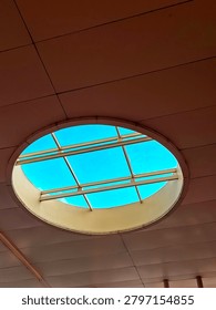 The architectural structure features smooth, large grey panels accented by a series of circular skylights that reveal a bright blue sky with subtle clouds.