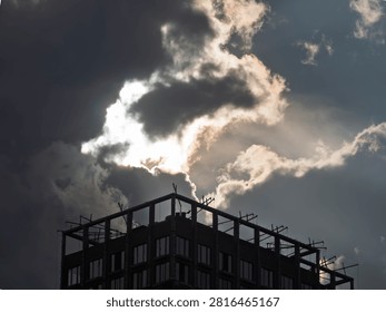 Architectural structure silhouette during sunset. A commercial building frame against a moody, dramatic sky with sun rays piercing through clouds.