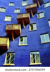 Architectural study of a tile clad concave exterior of an apartment building.  Windows and balconies in a diagonal stepped pattern.  Vibrant deep blue and yellow colour scheme. 