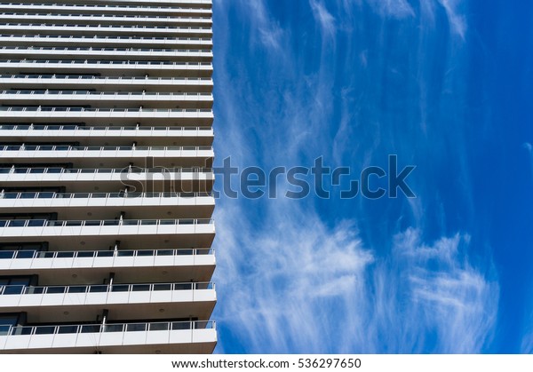 Architecture\
with blue sky on the background. Modern building with\
expressionless features against picturesque clouds on blue sky on\
the background. Nature VS man-made\
concept