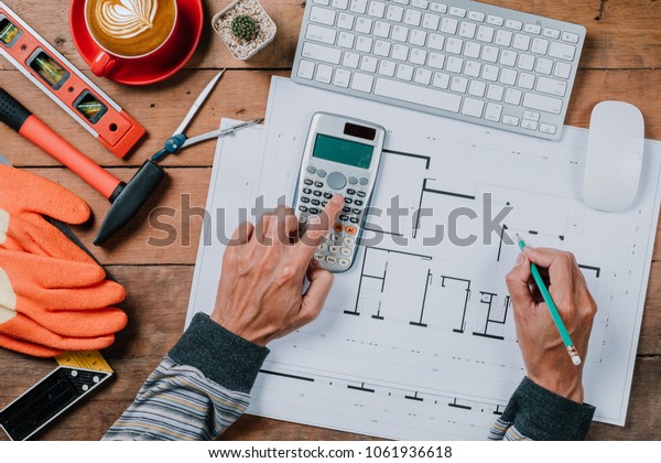 architecture, building,\
business, construction and people concept of architect hands\
working with calculator and pen on house blue print.Architecture\
concept.