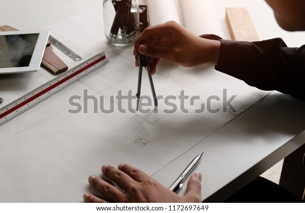 Architecture drawing on blueprint paper with\
dividers on hands.