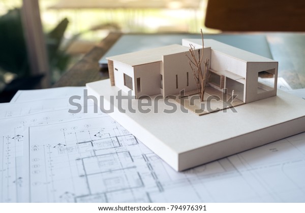 An architecture model\
with shop drawing paper and laptop on table in office with blur\
nature background