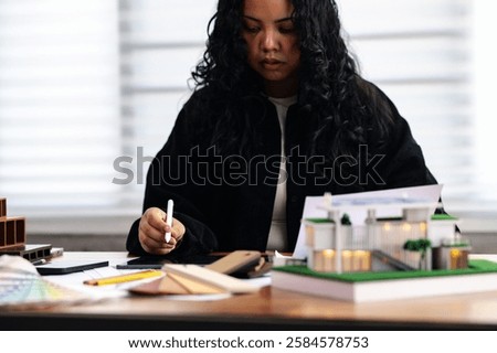 Architecture student uses tablet while reviewing interior drawing and material samples near a modern house model, Digital design and architectural planning. property development, building materials
