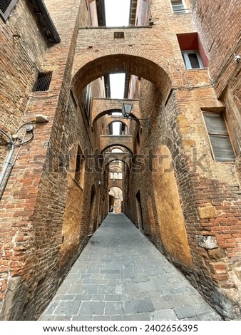 An archway constructed with red brick walls situated in a narrow alleyway in Siena. Tuscany, Italy.